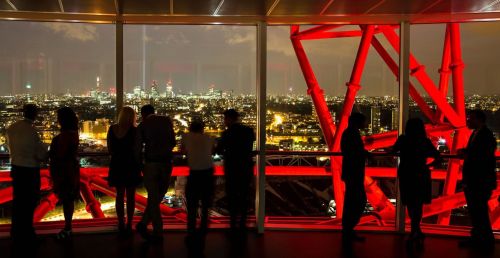Visitatori in controluce ammirano Londra di notte dall'ArcelorMittal Orbit, tra le travi rosse illuminate