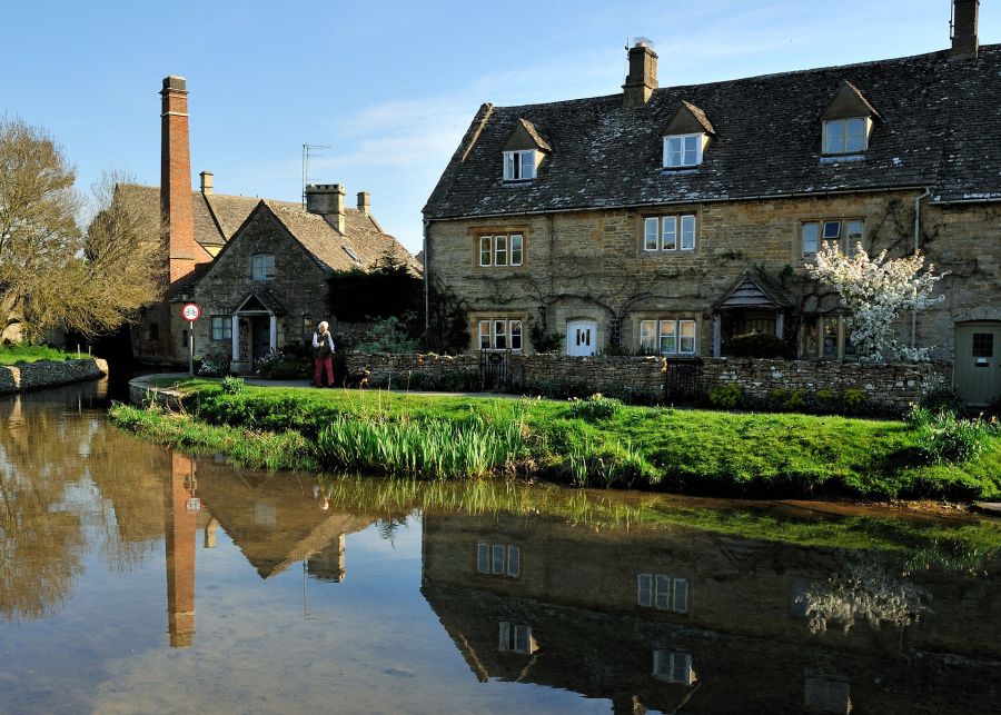Le case in pietra di Lower Slaughter riflesse nel fiume Eye, con la ciminiera del vecchio mulino sullo sfondo