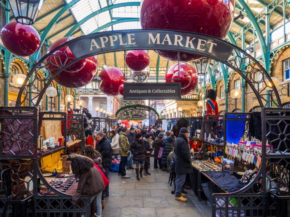 Grandi palle rosse appese sotto la copertura dell’Apple Market di Covent Garden, sopra le bancarelle e i visitatori