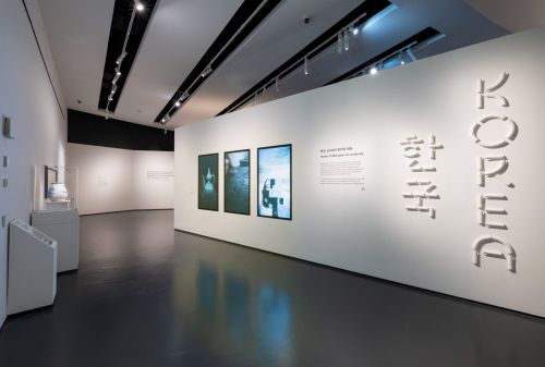 Sala d'ingresso della mostra Korea con parete del titolo bilingue e schermi con gli oggetti